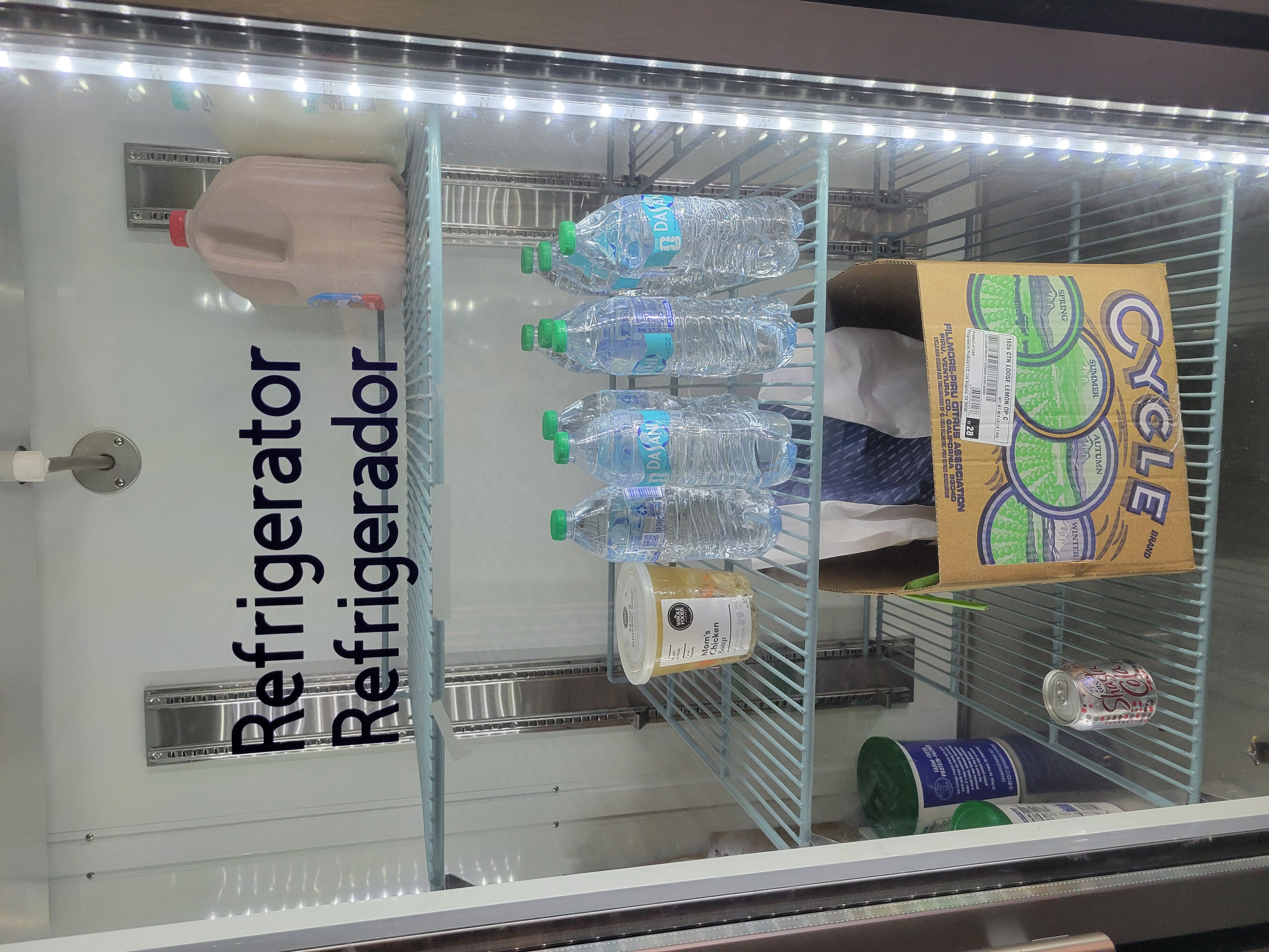 Gallon of chocolate milk, plastic container of chicken noodle soup, bottles of water, can of soda, and bag in a box in a fridge.